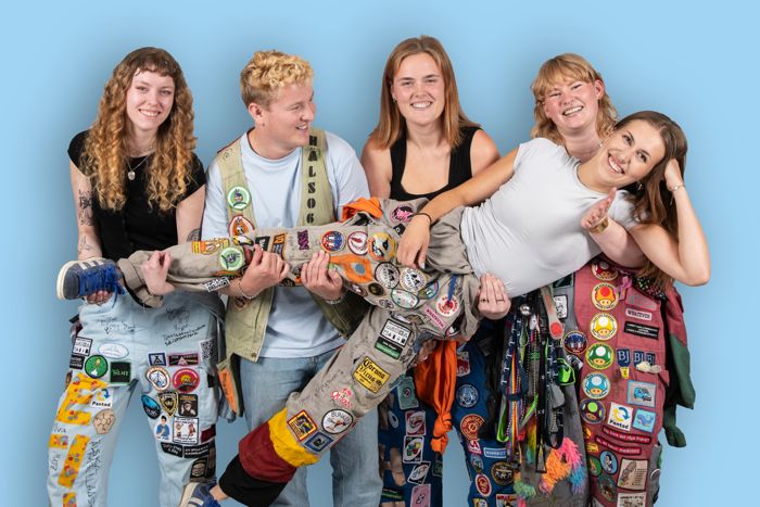 En grupp personer i studentoveraller som håller upp en liggande person i deras famnar