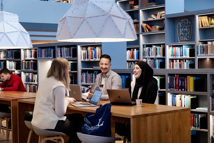 Tre personer som studerar i ett bibliotek