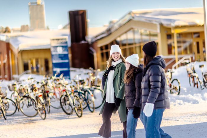 Three students walking on campus infront of the bicycle parking lot