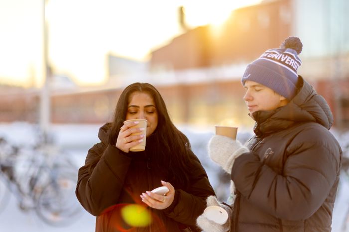 Two student outside in the snow enjoying coffee