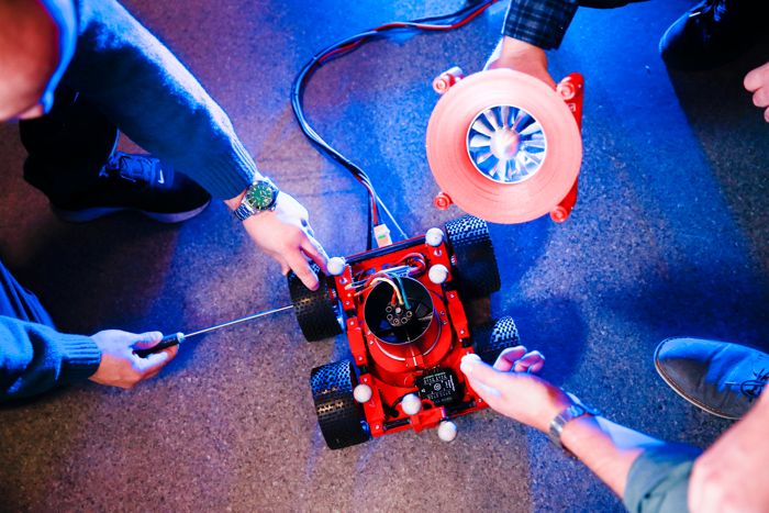 Personer som skruvar på en röd liten robot som syns i mitten av bilden.