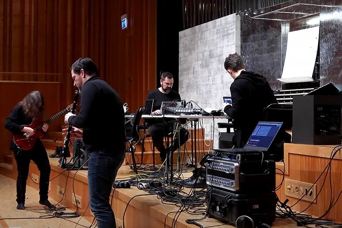 Tre män spelar på klarinett, elgitarr och dator med en orgel i bakgrunden